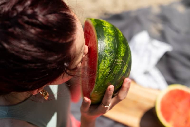 Person holding and smelling a fresh half-cut watermelon.