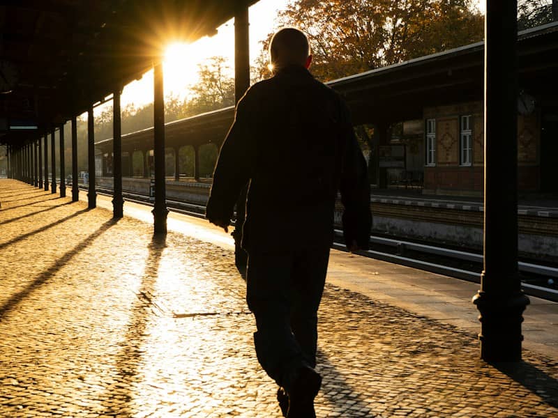 A man walking down a sidewalk next to a train station
