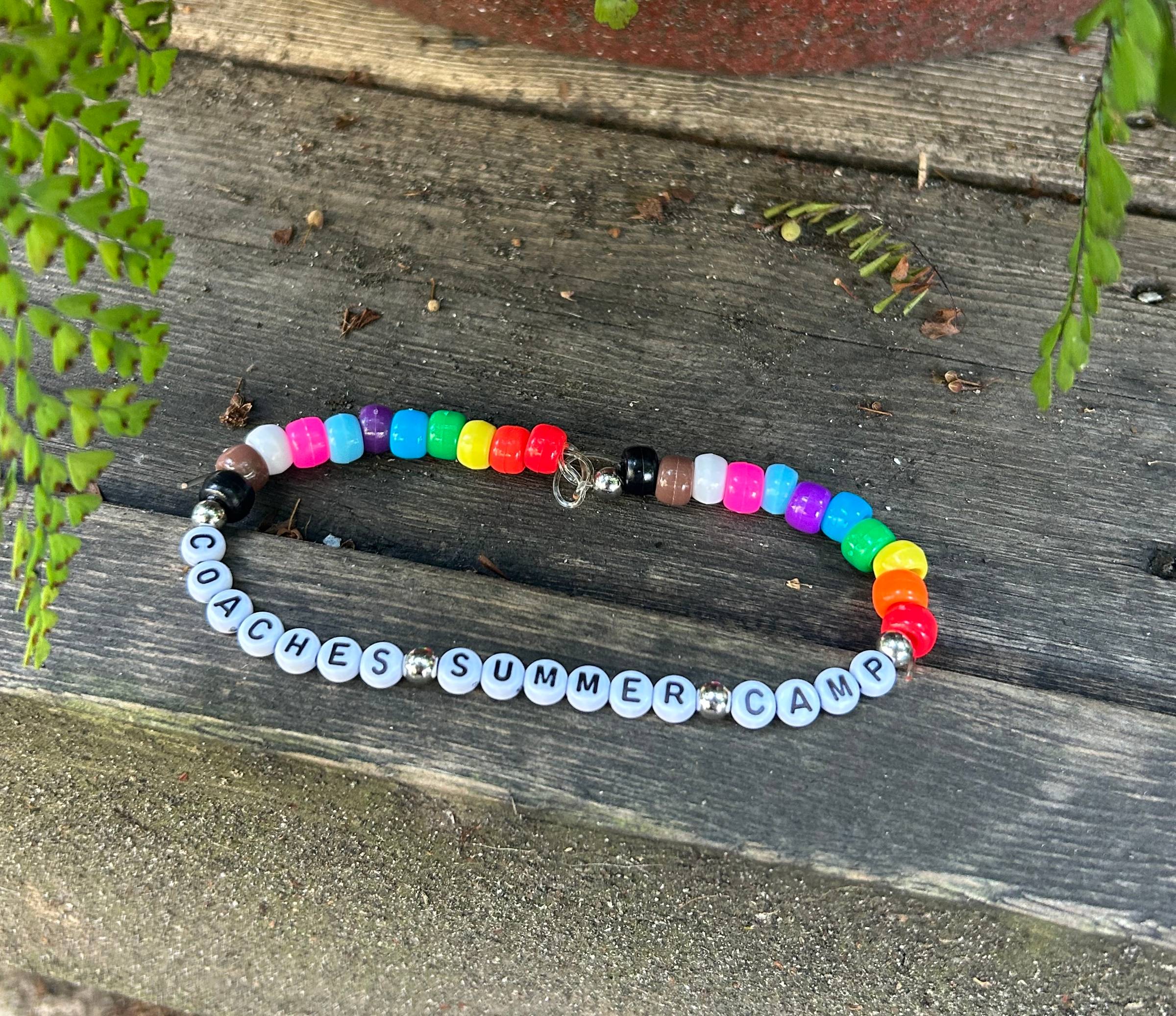 friendship bracelet that says "coaches summer camp" with rainbow coloured beads