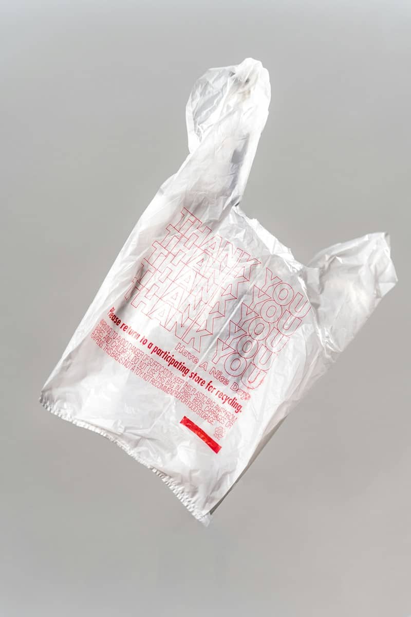 A white plastic shopping bag with red text floating against a grey background