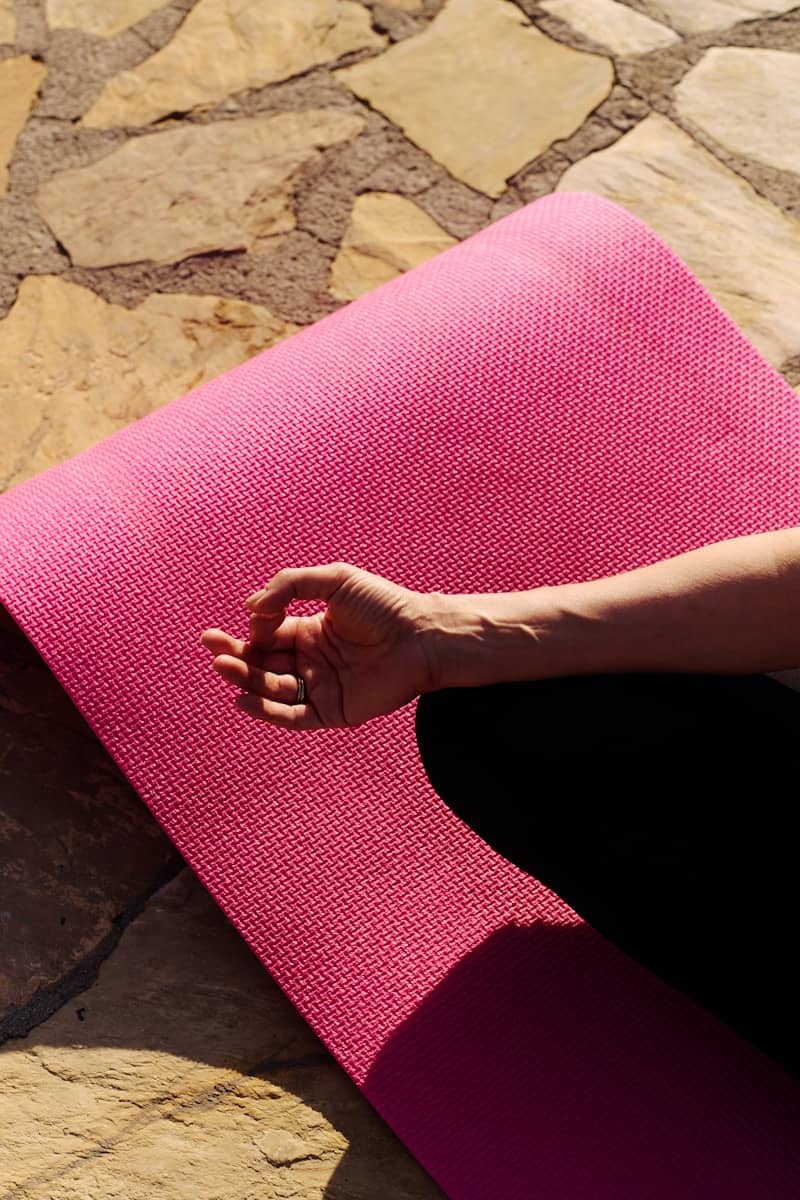 A hand rests on a pink yoga mat.