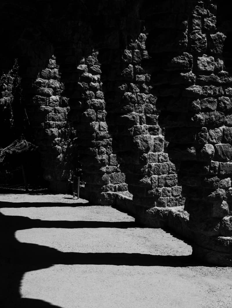 A stone colonnade casting long shadows across a gravel path in bright sunlight