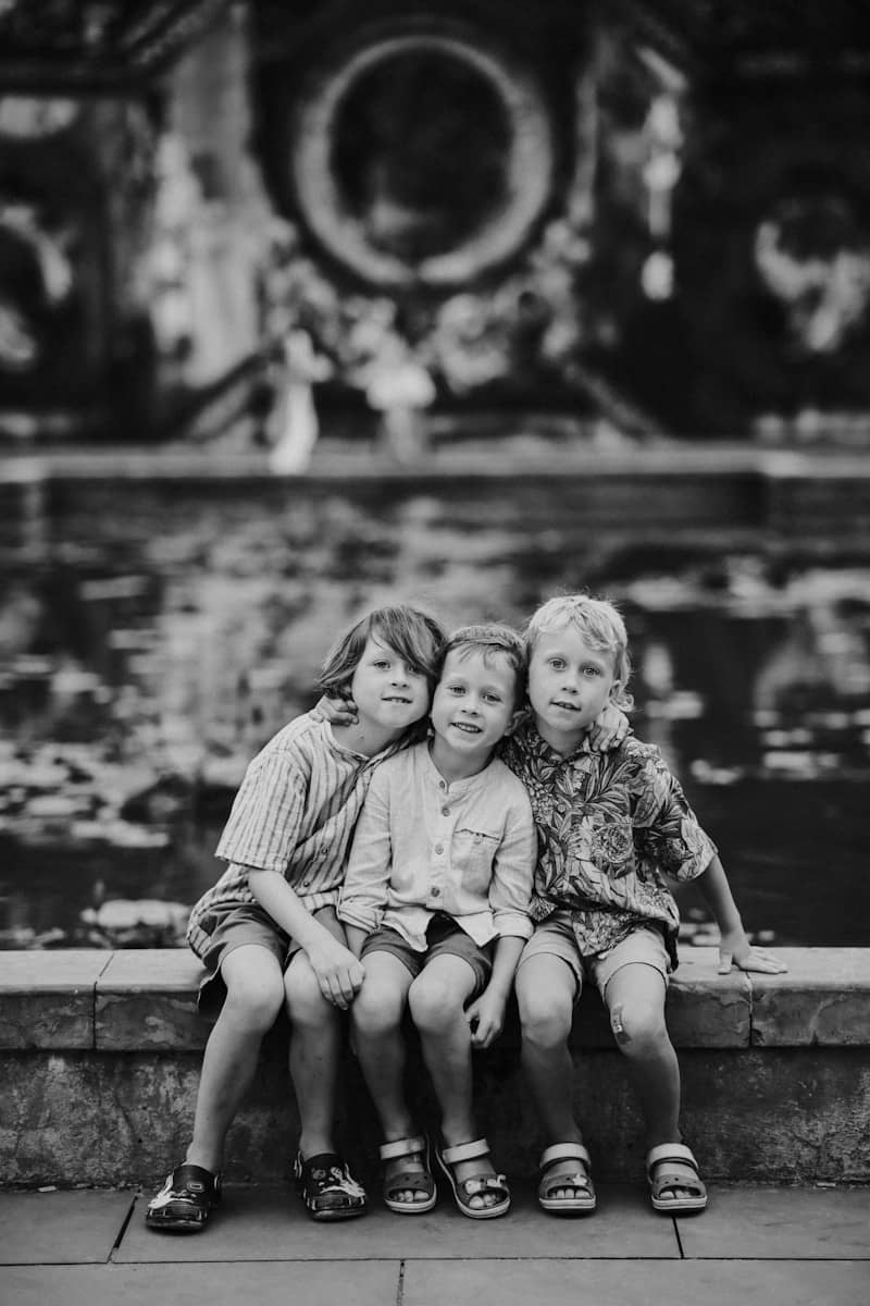 Three young boys sit together in front of a fountain.