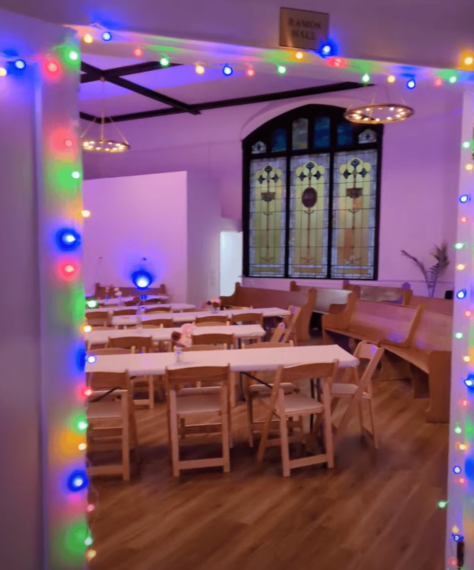 A room with tables, chairs, and stained glass windows, with a twinkly lights threshold