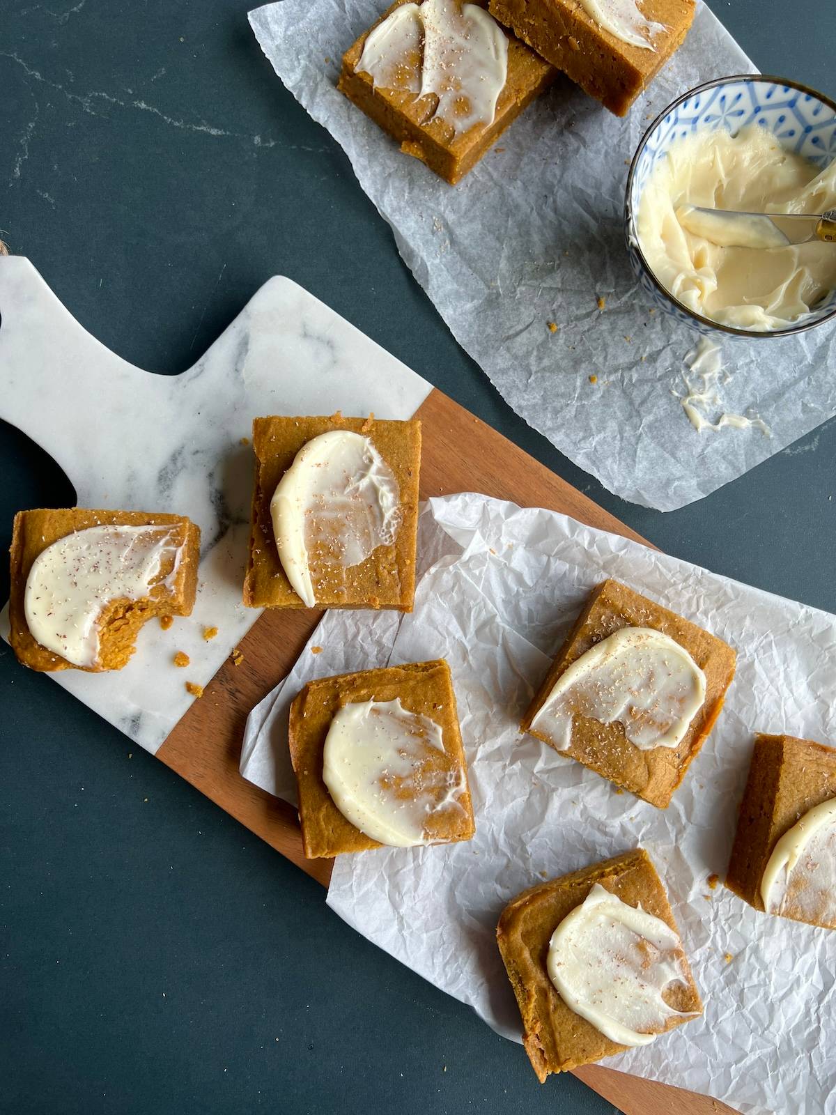 pumpkin spice blondies are topped with swirls of cream cheese frosting and arranged on a serving board