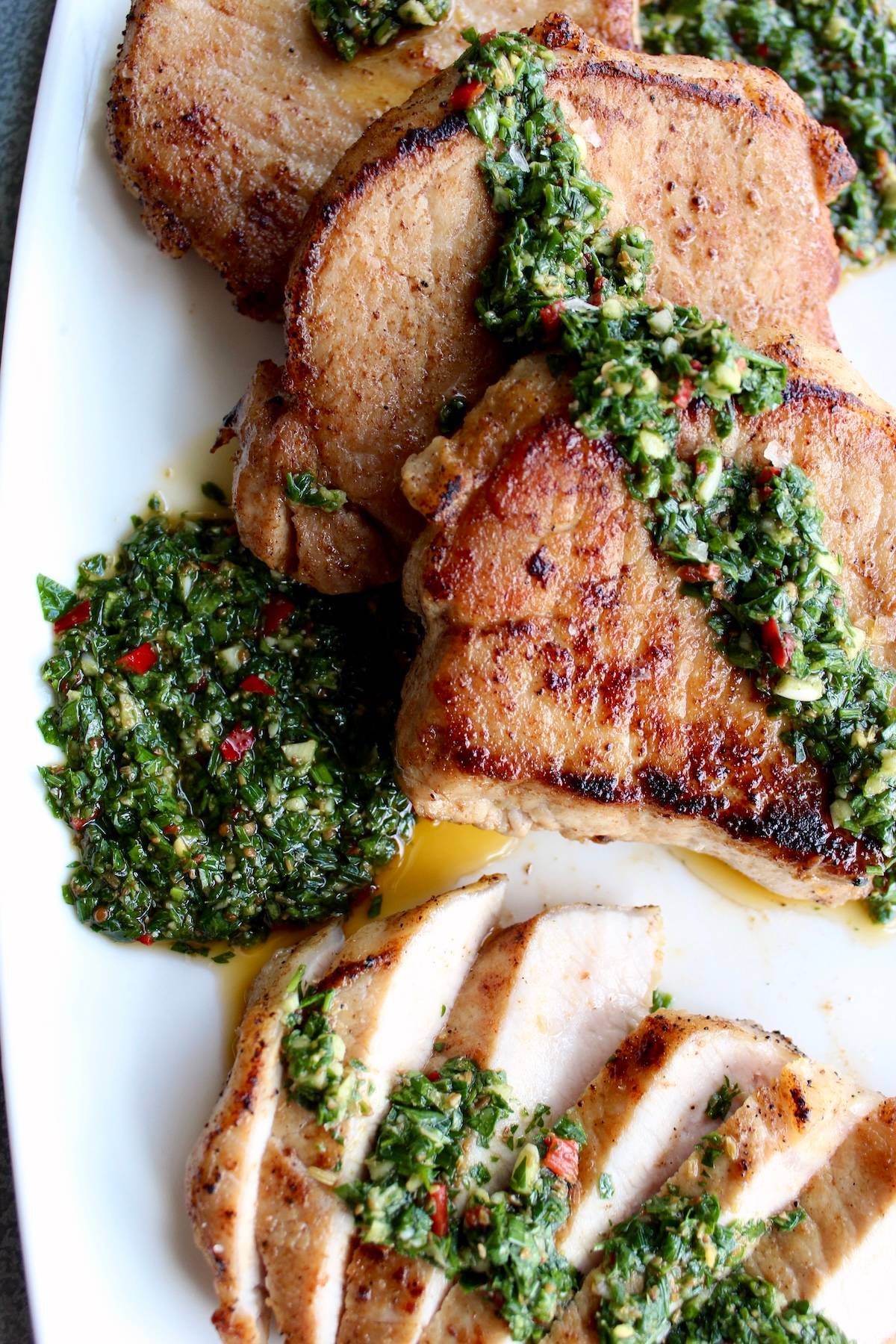 seared pork chops are sliced and drizzled with fresh chimichurri sauce