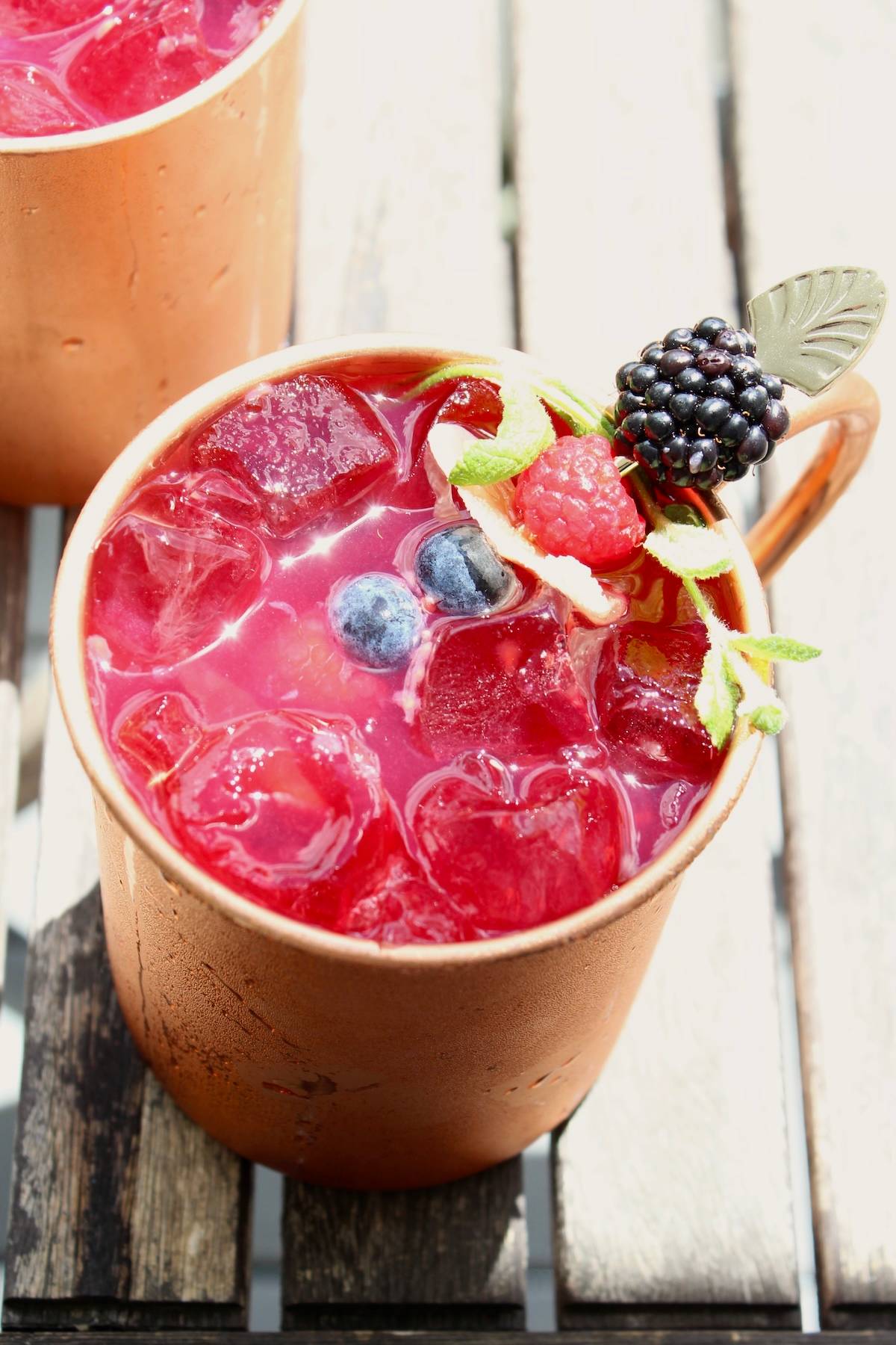 a berry moscow mule cocktail sitting on a patio table in the sun