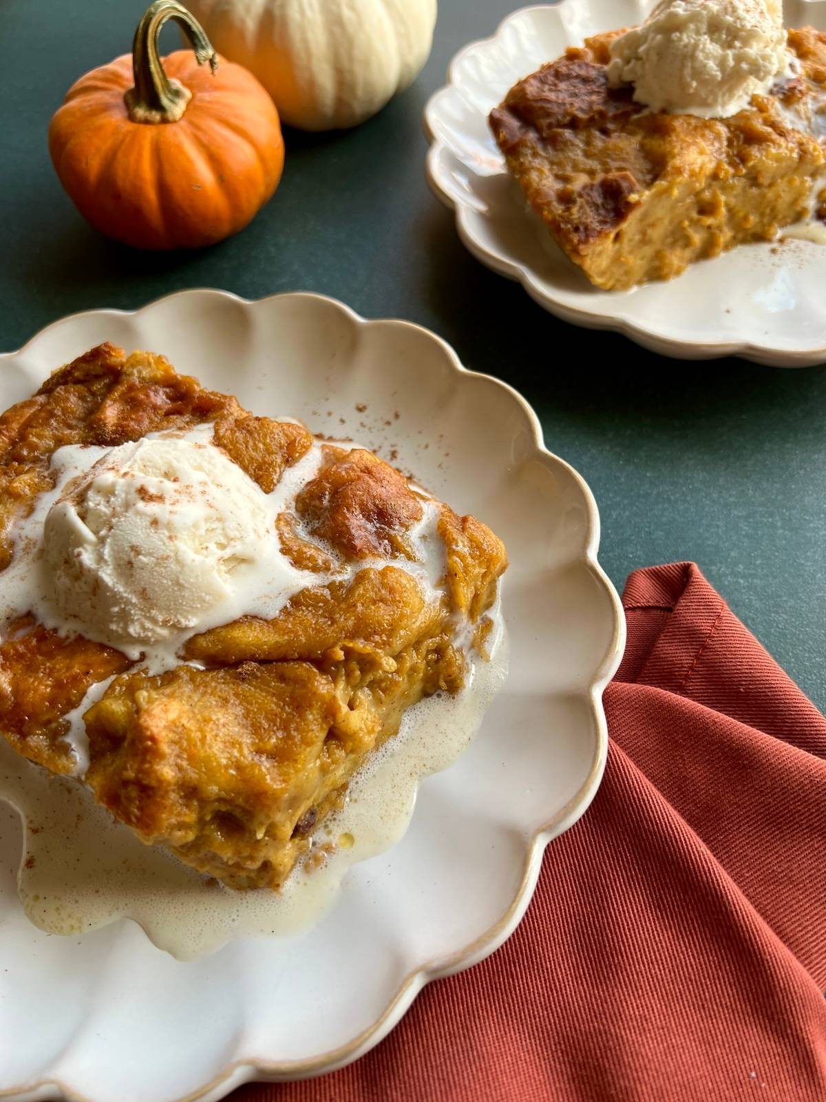 two plates of pumpkin brioche bread pudding are topped with vanilla ice cream