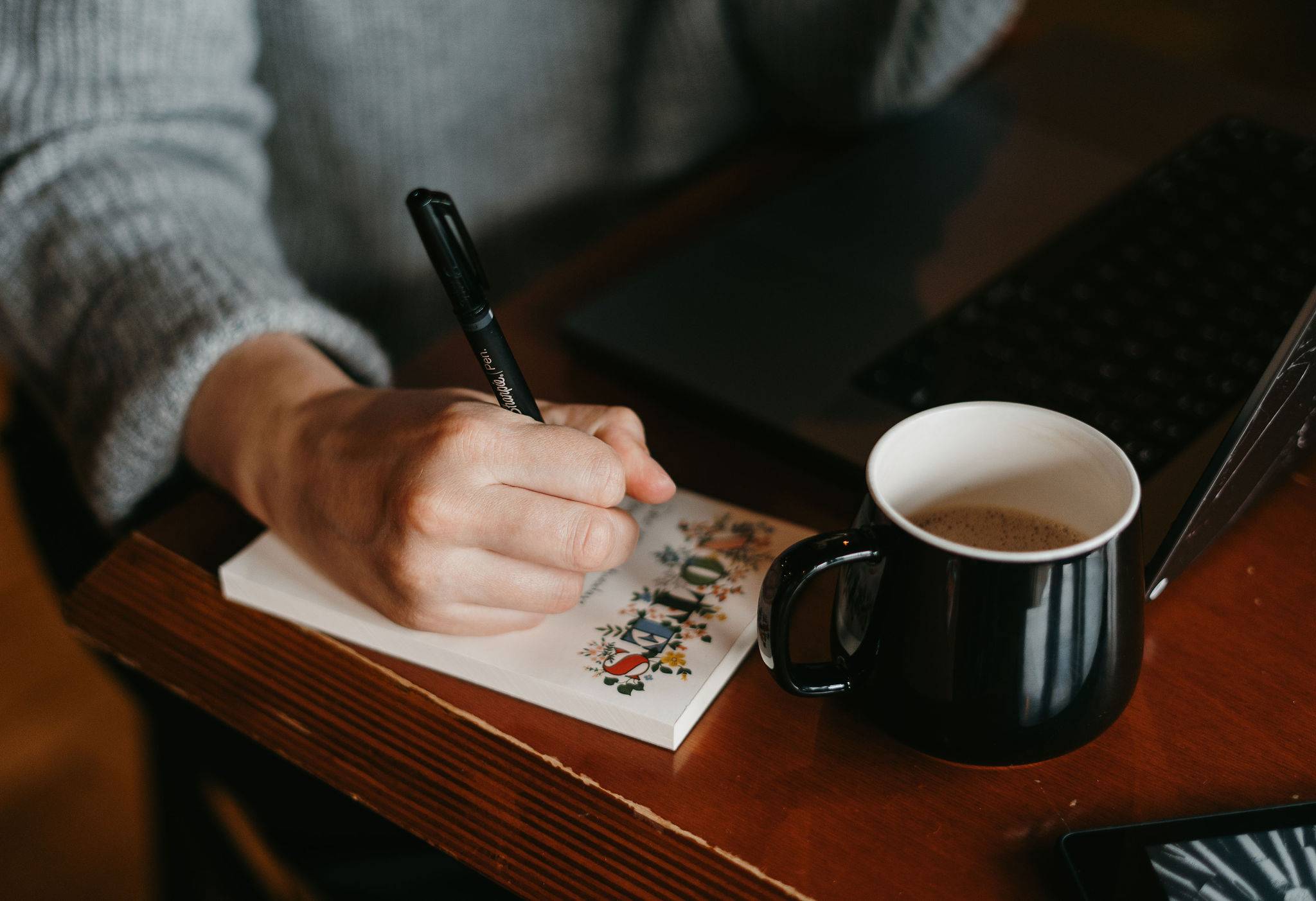 A stack of books, a notepad, an e-reader, and a coffee cup sit on a wooden bench.