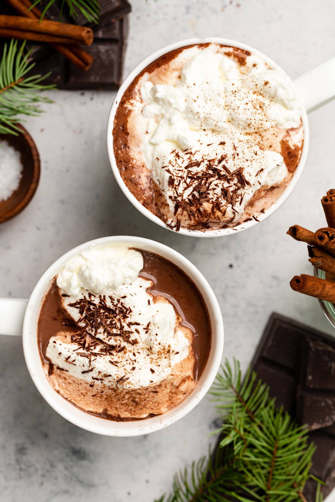 two cups of hot cocoa topped with whipped cream and chocolate shavings