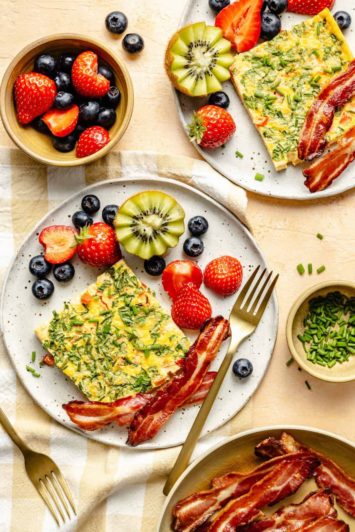 sheet pan eggs on a plate with fork, bacon, and fruit