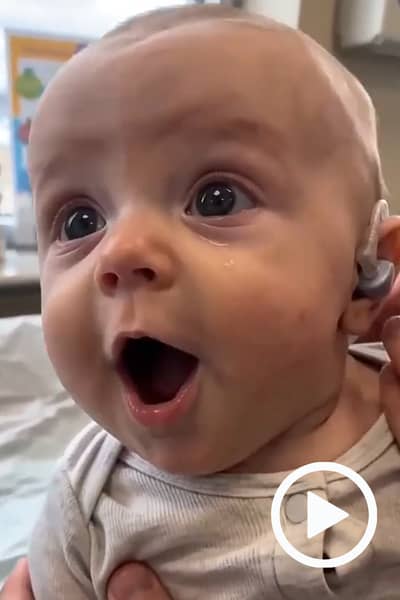 Video: a baby wearing a hearing aid, eyes wide and mouth open in surprise.