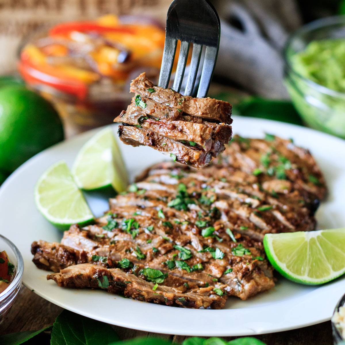 forkful of Chipotle carne asada with lime wedges.