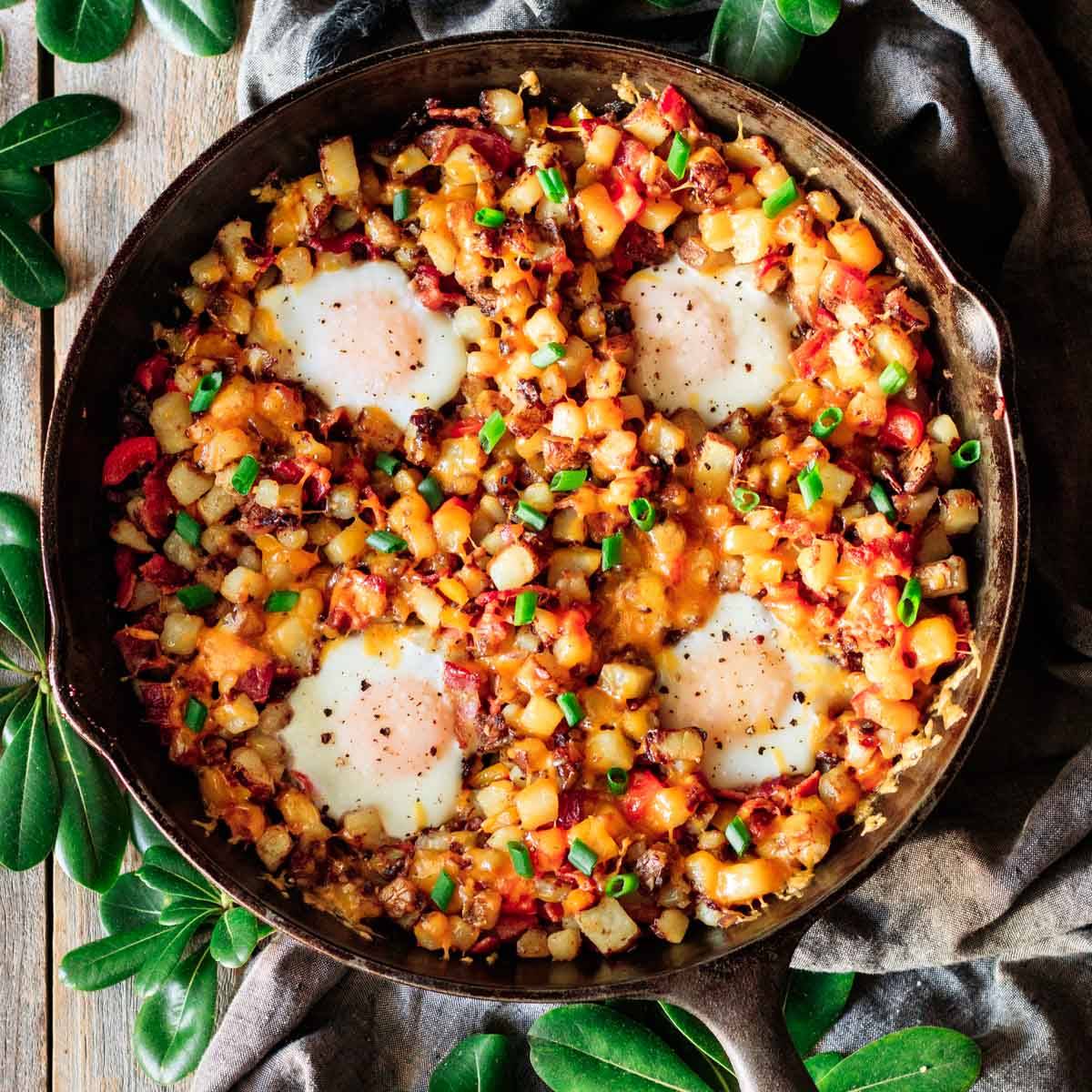 cast iron skillet filled with diced potatoes, veggies, and eggs.