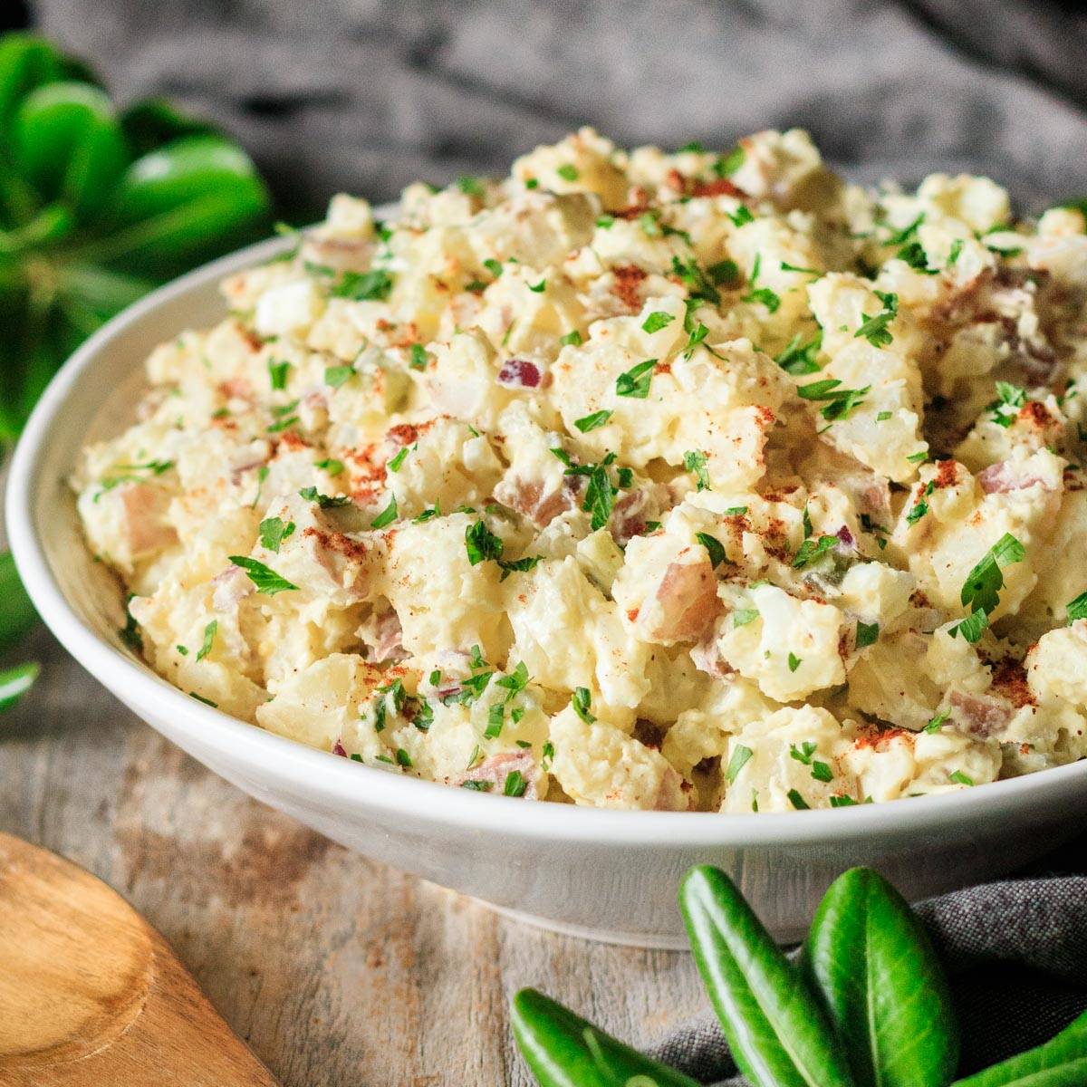 white bowl of potato salad with a wooden spoon.