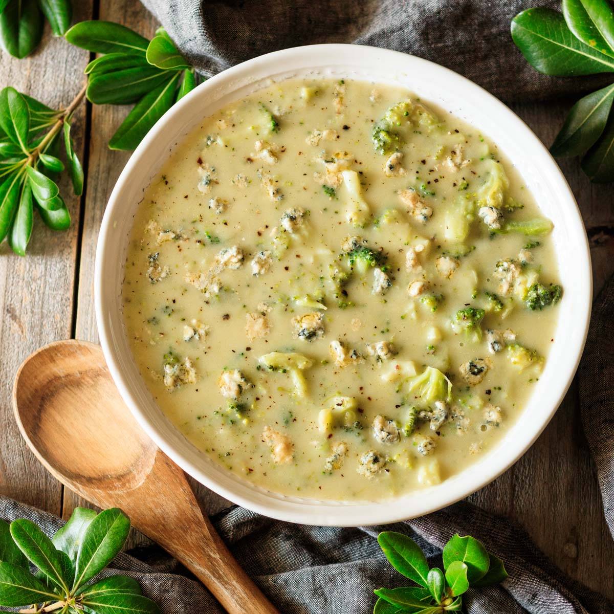 white bowl of broccoli & stilton soup with a wooden spoon.