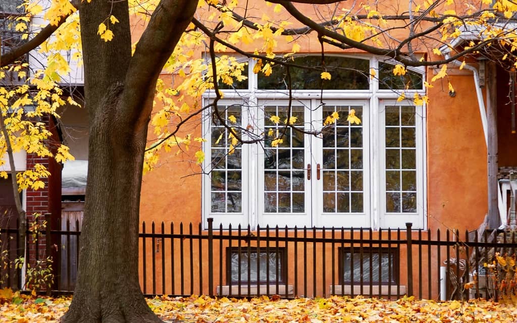 Orange colonial home covered in yellow and orange leaves on an autumn afternoon