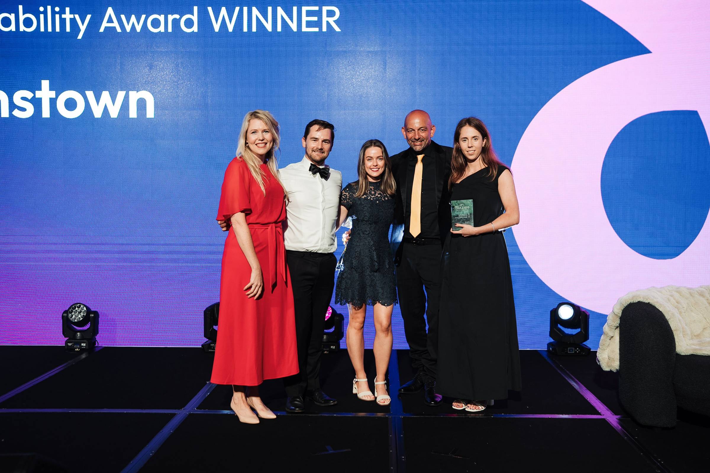 Five people in formalwear standing on a stage with "Winner" in the background
