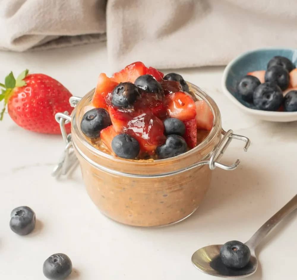 Close-up of almond butter and jam overnight oats with toppings in a jar.
