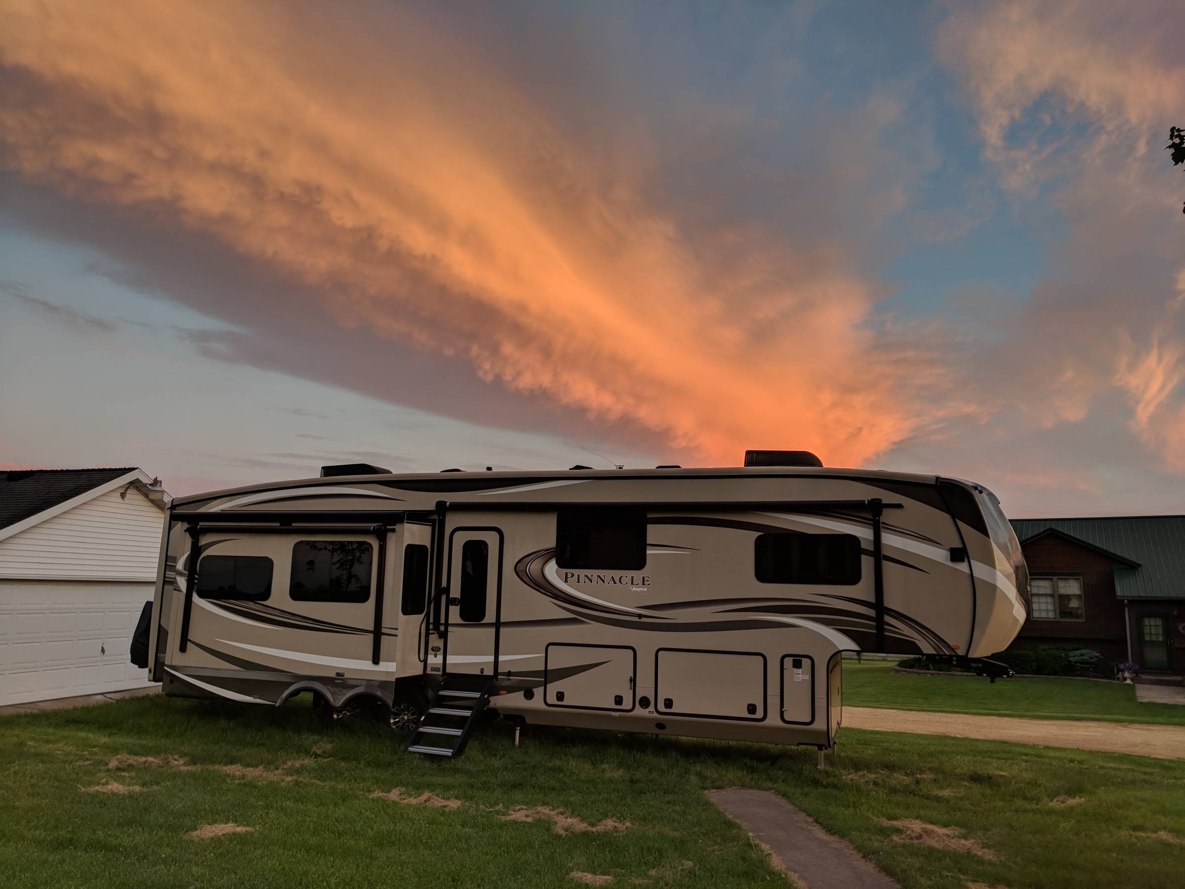 A large fifth wheel RV is parked on family property while moochdocking, with a dramatic orange and pink sunset stretching across the evening sky overhead. This family travel and RV living moment highlights one of the benefits of moochdocking by staying wi