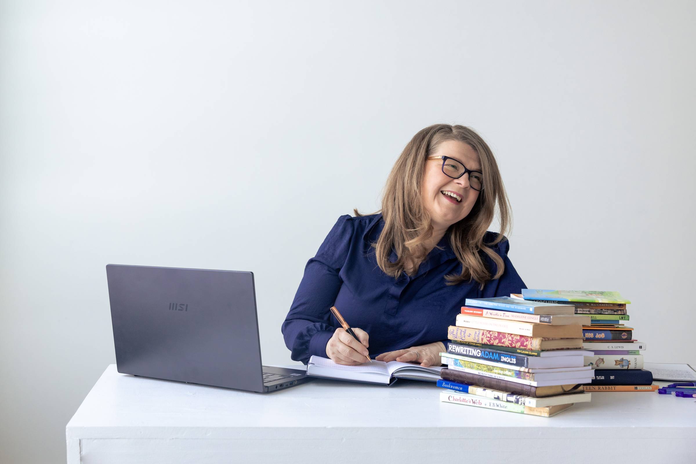 Colleen McCubbin writing and laughing at a table full of books and a computer.