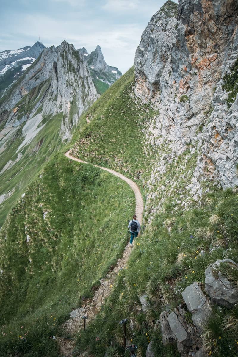 Hiker on a narrow winding trail along a steep mountain.