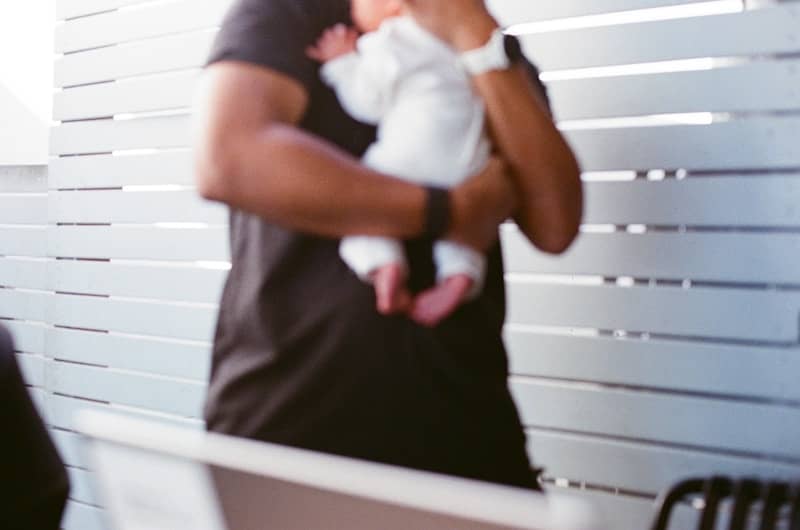 A person holds a baby in a white outfit.