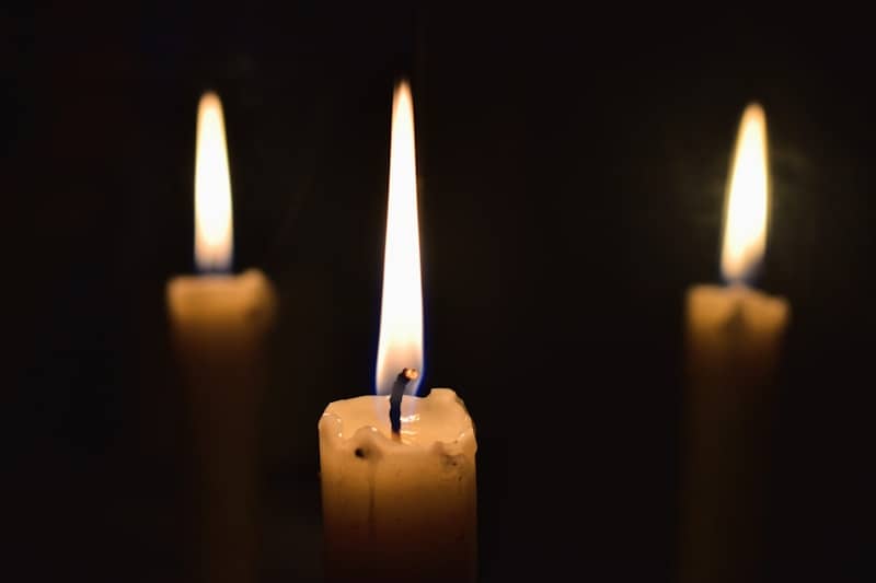 Three lit candles against a dark background.