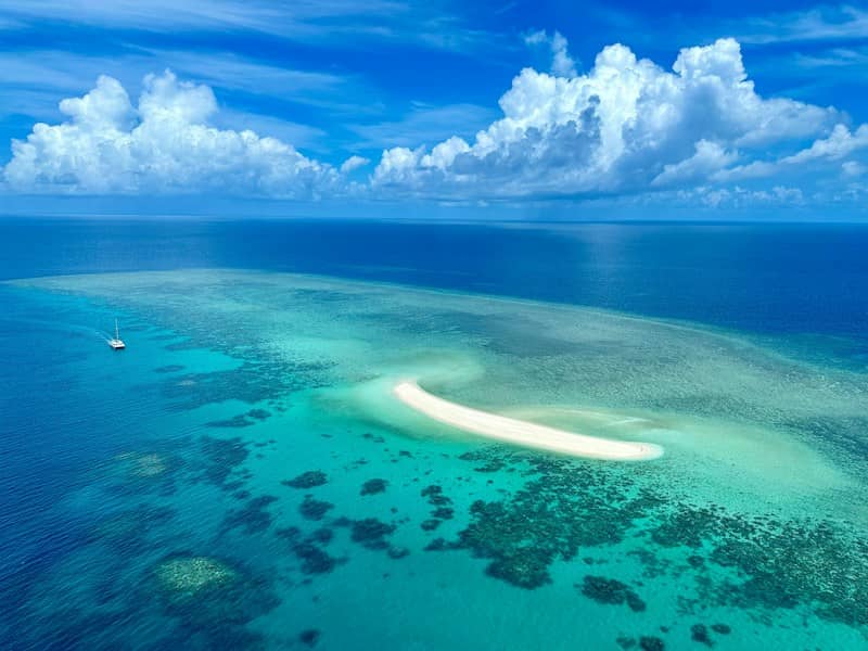 Aerial view of a white sandbar in turquoise water with a small boat