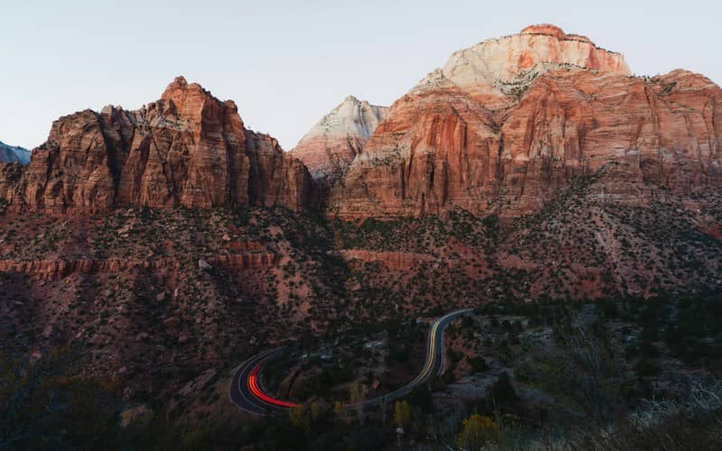 A winding road with light trails below towering red sandstone cliffs in Zion National Park