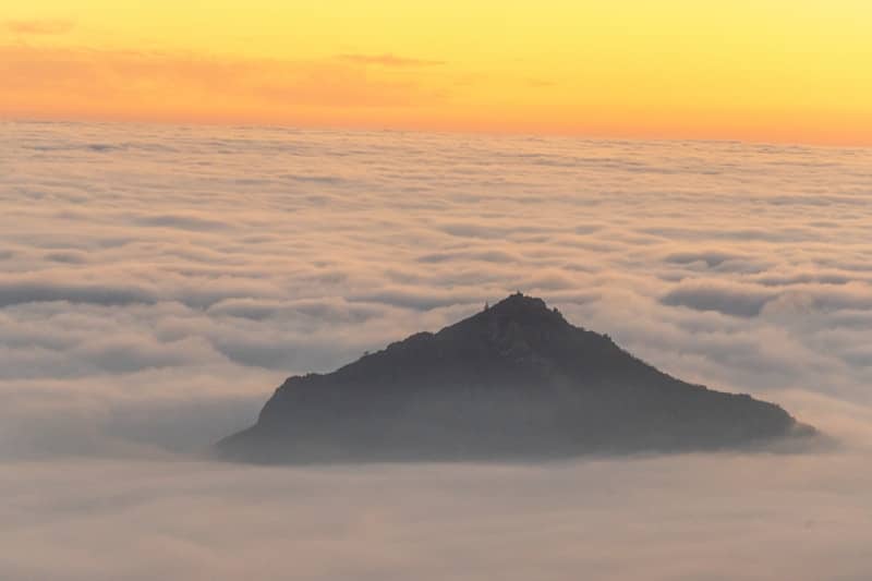 Mountain peak emerging from a sea of clouds at sunrise.