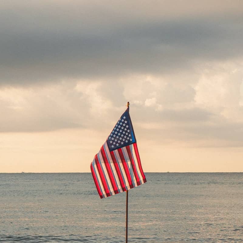 An american flag waves against a cloudy sky and ocean.