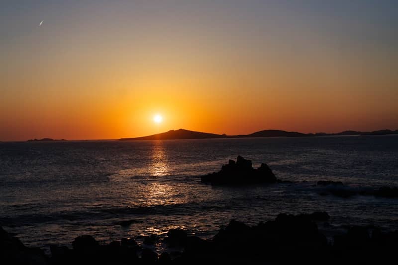 Golden sunset over ocean with islands and dark rocks.