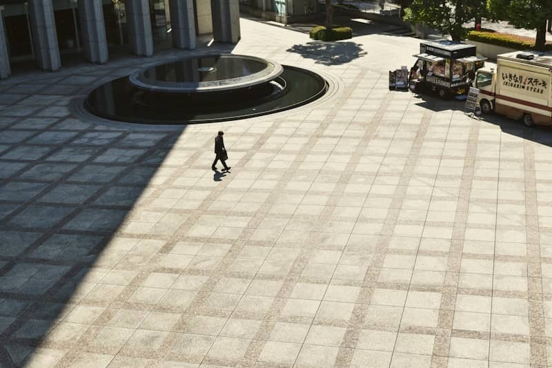 A person walks across a sunny plaza.