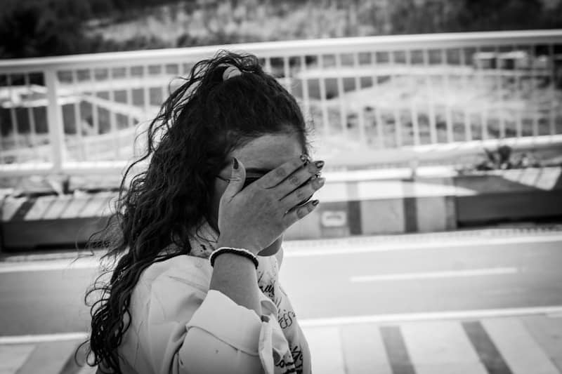 Woman with curly hair covering her face on a bridge.