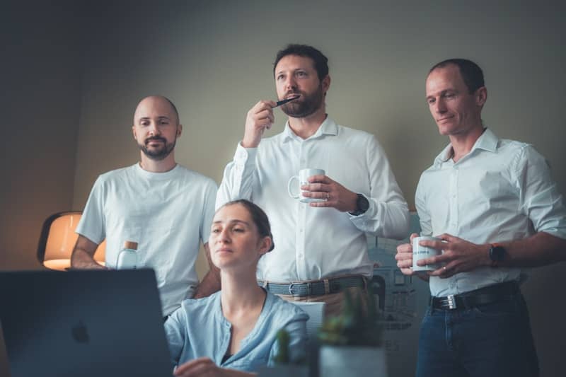 Four people in a room looking at a laptop.