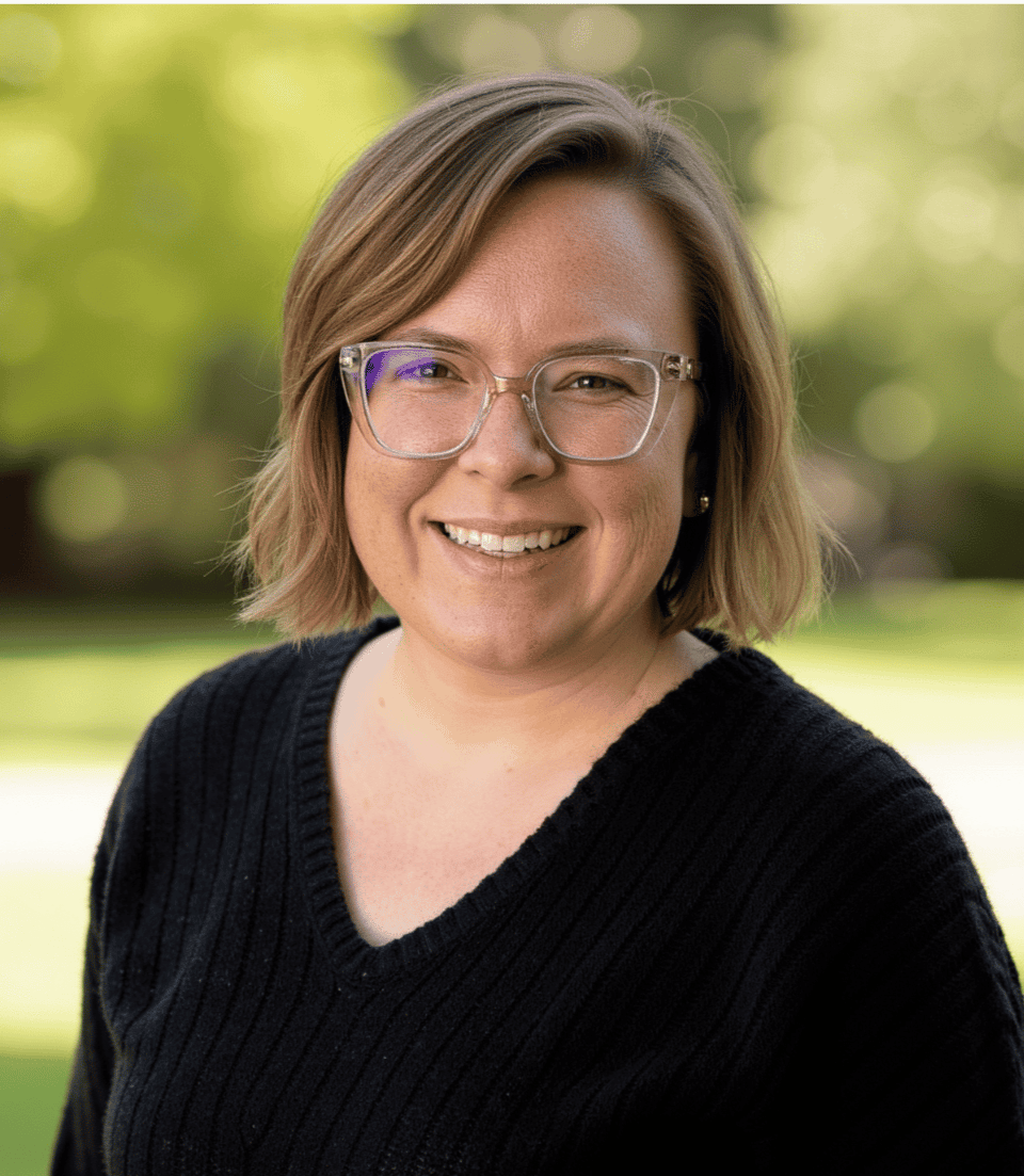 ```plaintext
A promotional flyer featuring a smiling woman with glasses standing outdoors in front of a blurred background of trees and grass. Below her photograph, text introduces Dr. Elizabeth "Liz" Polinsky as a certified Emotionally Focused Therapy supervisor and therapist for individuals, couples, and families. She is the founder of Communicate & Connect Counseling. Her interests include swing dancing, making wine, and hosting a podcast for military relationships. Two logos are at the bottom: one for the APA and one labeled GPA.
```