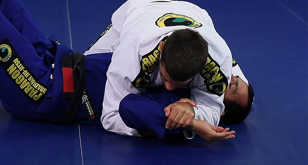 Smaller Brazilian jiu-jitsu grappler defending underneath a much larger training partner on the mat.
