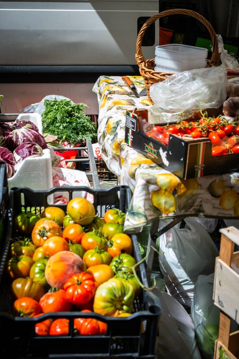 A black crate filled with heirloom tomatoes beside a table with fresh produce