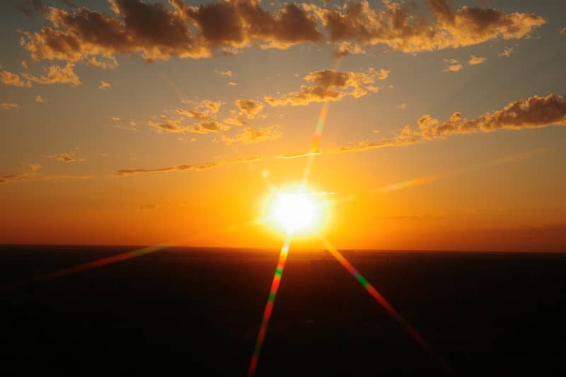 Golden sunset with bright sunburst and scattered clouds.