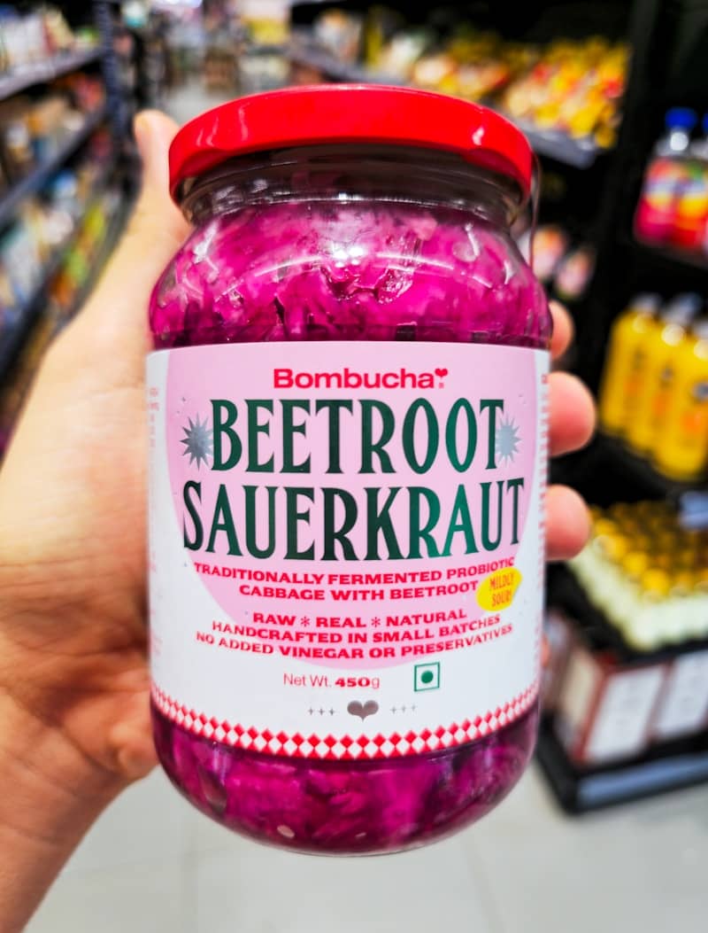 Hand holds jar of beetroot sauerkraut in store.