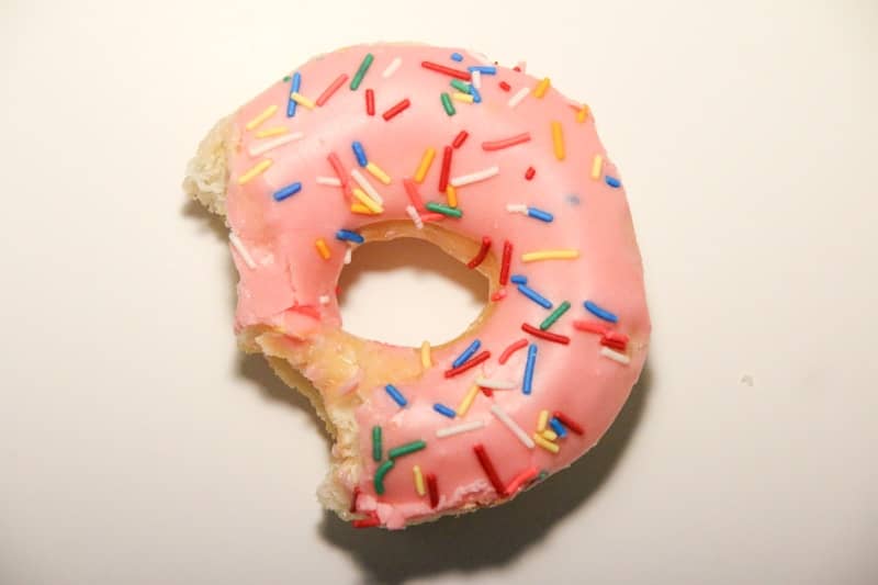 A partially eaten pink donut with colorful sprinkles