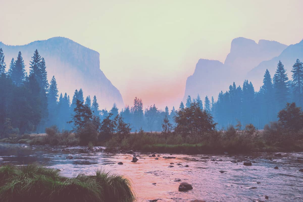 A river winding through Yosemite Valley, flanked by massive granite cliffs and illuminated by soft afternoon light.