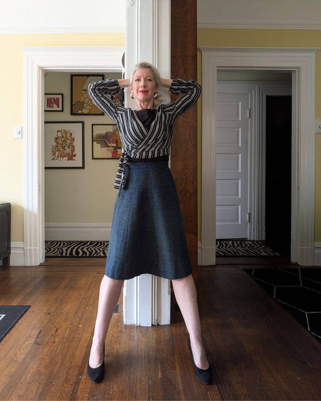 woman in skirt and striped top leaning back on wall with arms behind head