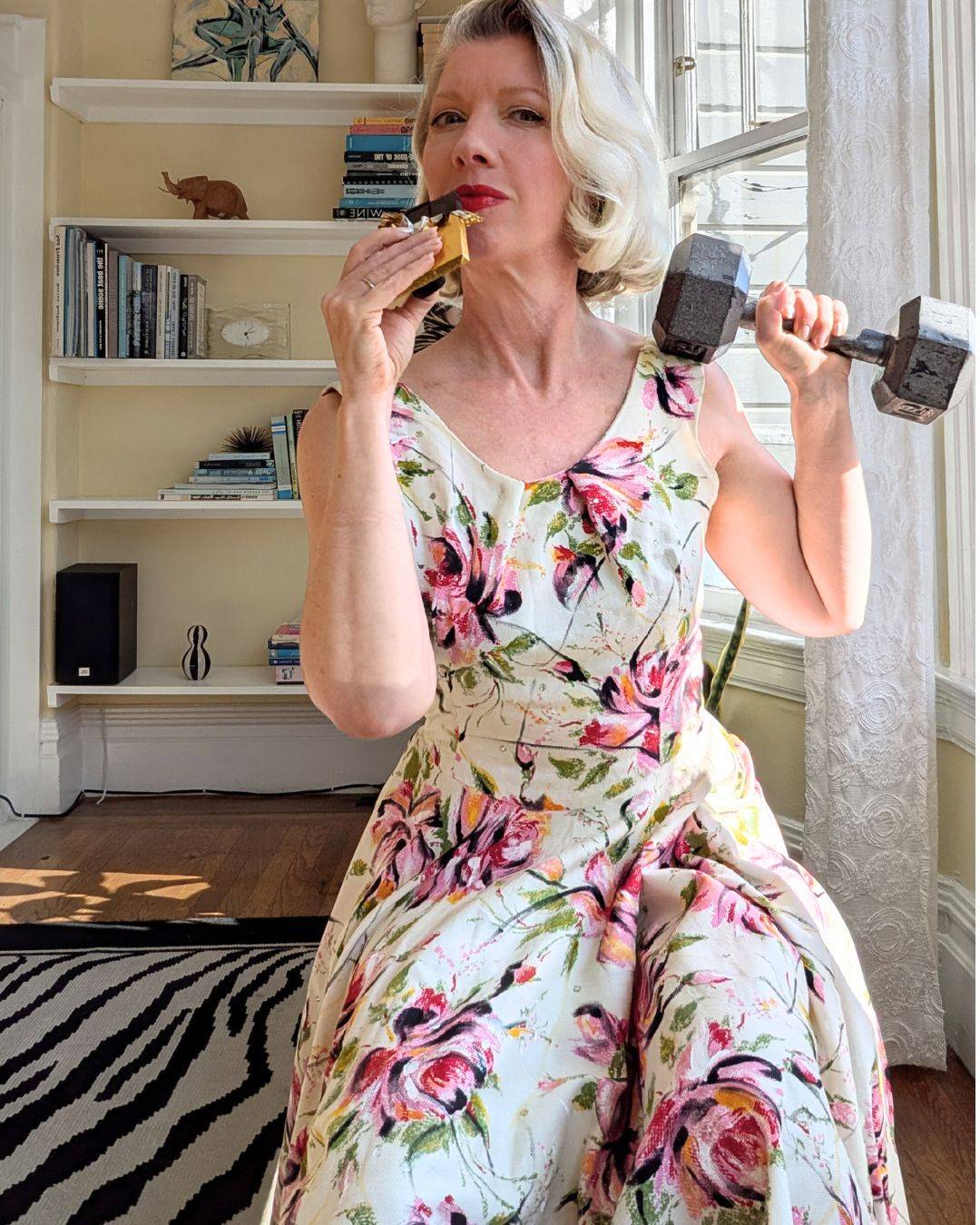 woman in floral dress eating chocolate while holding a dumbbell