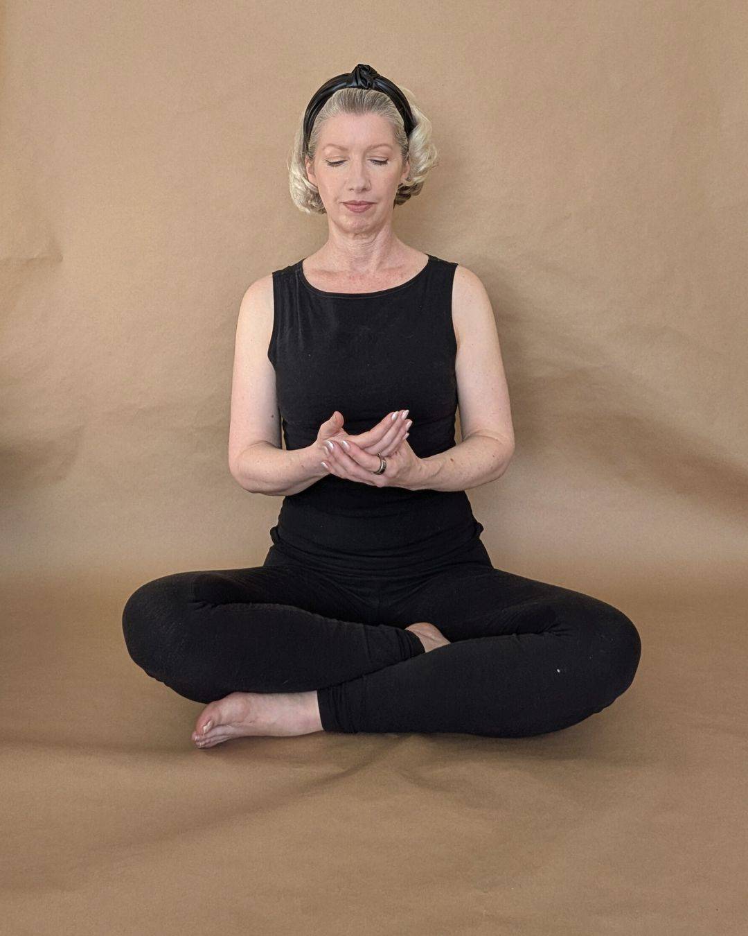 woman in black meditating cross-legged on floor