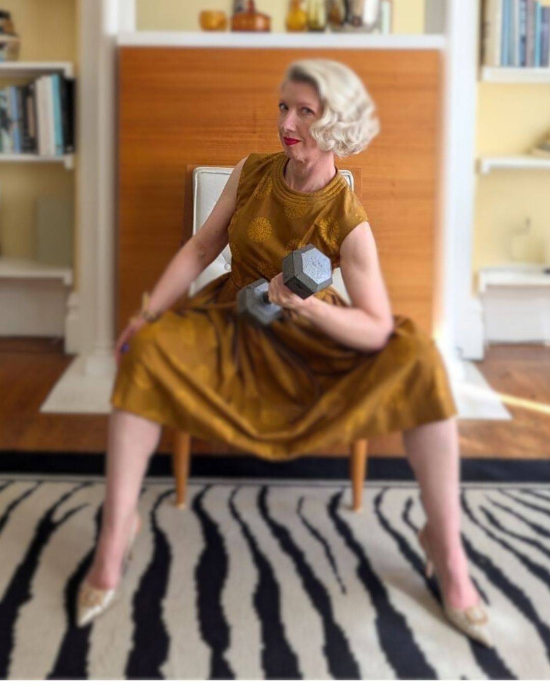 blonde woman in gold vintage dress doing a bicep curl