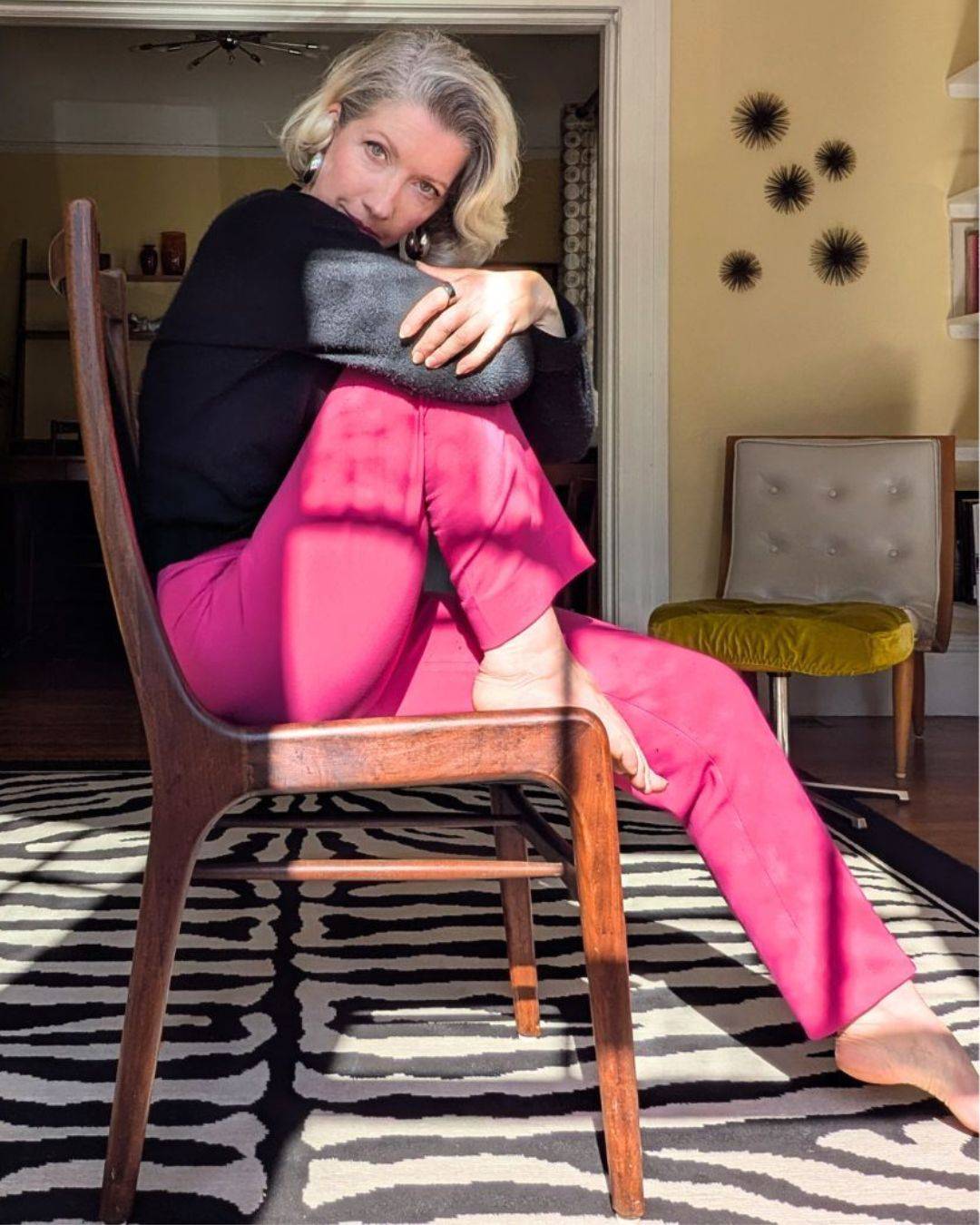 woman in pink pants sitting on sideways on chair