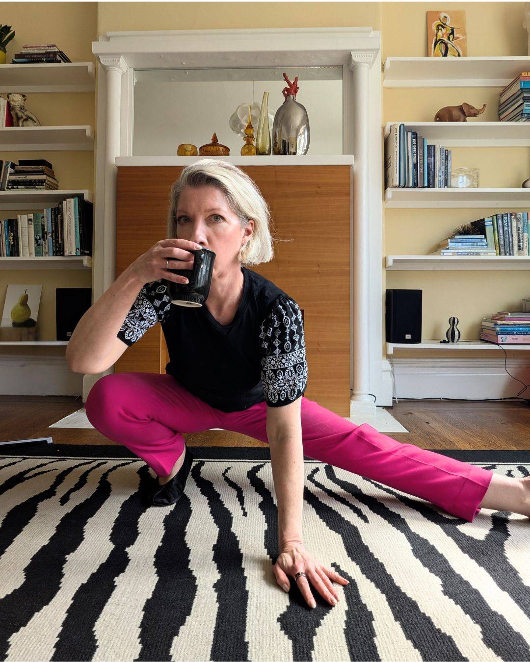 blonde woman in pink pants in low side lunge sipping coffee