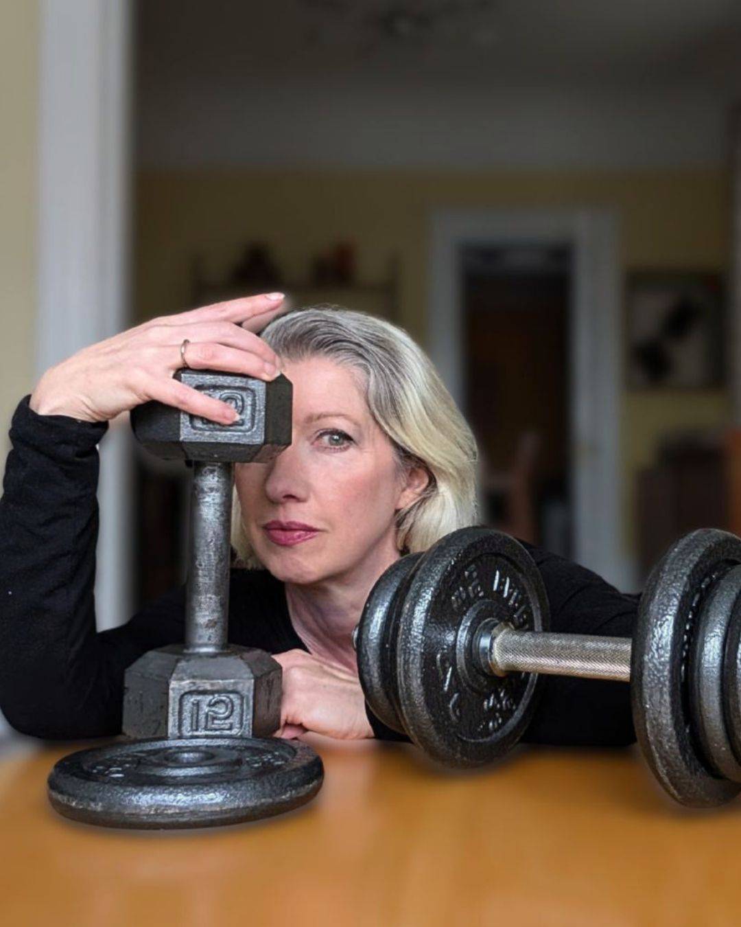 dumbbells in foreground with blonde woman looking through them